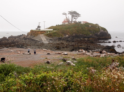 [The two story lighthouse sits on a small land mass which becomes an island during higher tides. At low tide there is a pathway across the land to the mainland. A paved drive comes down the island to the approximate point of the high tide.]